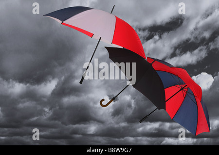 Trois parapluies d'être soufflé dans un sombre ciel nuageux orageux Banque D'Images