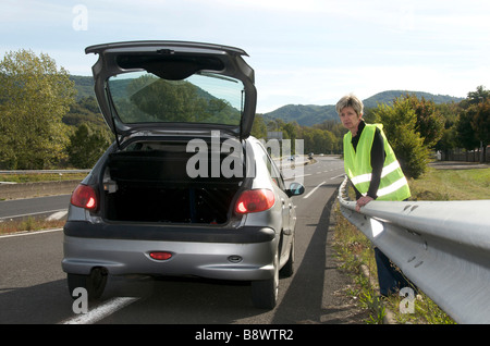 Femme debout derrière la barrière armco avec sa voiture en panne en attente de l'aide sur une bretelle autoroute Banque D'Images