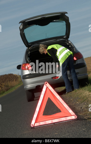 Femme avec son ventilées voiture garée au bord de la route le port de haute visibilité jaune / Hi Viz jacket et le triangle Banque D'Images