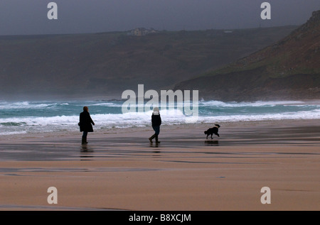 Deux personnes marcher un chien sur la plage de Sennen à Cornwall le un jour brumeux. Banque D'Images