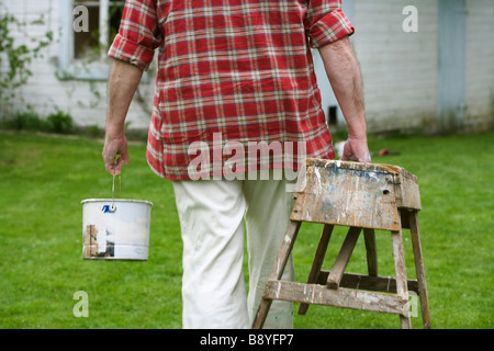 Un homme avec un chevalet et une bouteille de peinture marche dans un jardin. Banque D'Images