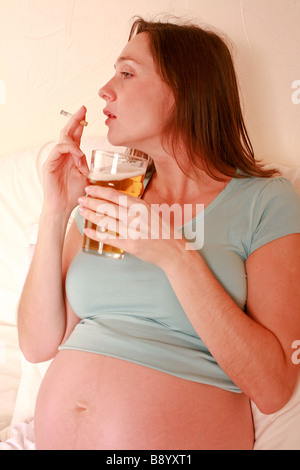 Femme enceinte de boire pinte de bière en verre d'alcool et plus de cigarettes Fumer nuit à foetus baby smiling mauvais régime health Banque D'Images