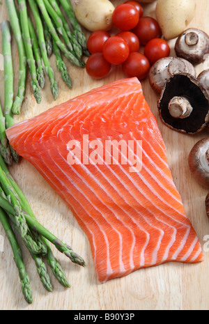 Un pavé de saumon cru sur une planche avec les asperges champignons tomates cerises et pommes de terre Banque D'Images