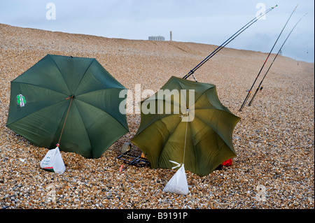 Deux pêcheurs de la mer de la plage de galets à l'aide de leur parapluie comme brise-vent sur Dengemarsh Beach, Dungeness, dans le Kent, UK Banque D'Images