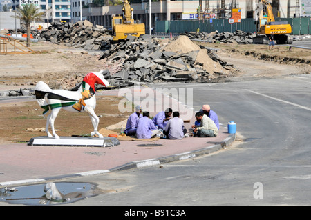 Scène de rue de Dubaï à l'industrie de construction de bâtiment groupe de site de Pause repas des travailleurs assis sur le trottoir avec statue de cheval unie Émirats arabes Unis Banque D'Images