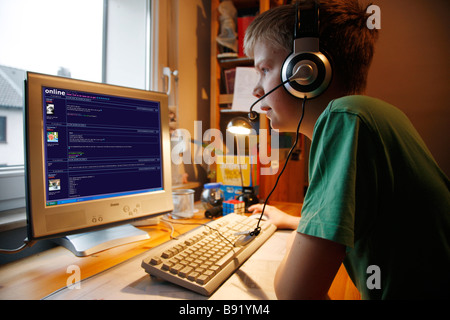 Un garçon, 13 ans, est en pleine discussion dans sa chambre de l'enfant et parle à un chat membre par la voix sur IP. Il porte un casque. Banque D'Images