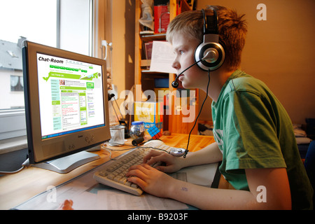 Un garçon, 13 ans, est en pleine discussion dans sa chambre de l'enfant et parle à un chat membre par la voix sur IP. Il porte un casque. Banque D'Images