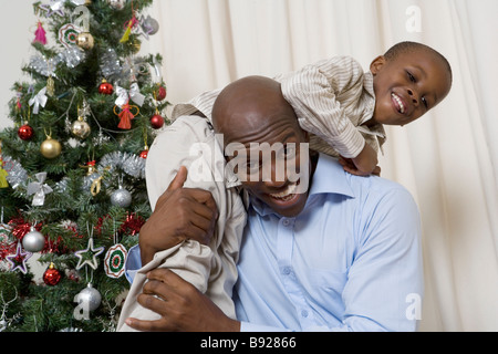 Père ramasser son fils jusqu'au-dessus de son épaule debout à côté d'un arbre de Noël Banque D'Images