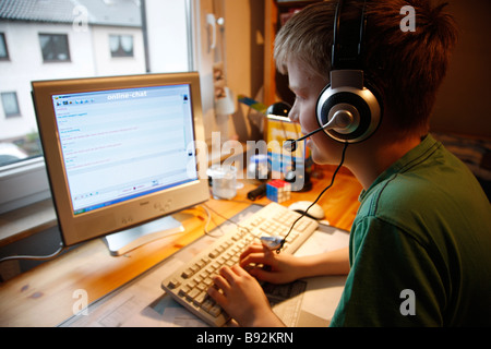 Un garçon, 13 ans, est en pleine discussion dans sa chambre de l'enfant et parle à un chat membre par la voix sur IP. Il porte un casque. Banque D'Images