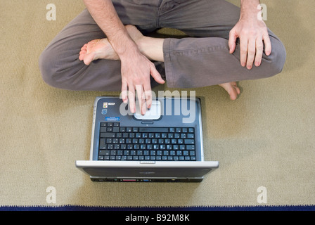 Homme assis les jambes croisées sur le plancher à l'aide d'ordinateur portable Banque D'Images