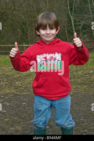 Jeune garçon gallois dans dragon rouge bleu jeans giving thumbs-up Banque D'Images