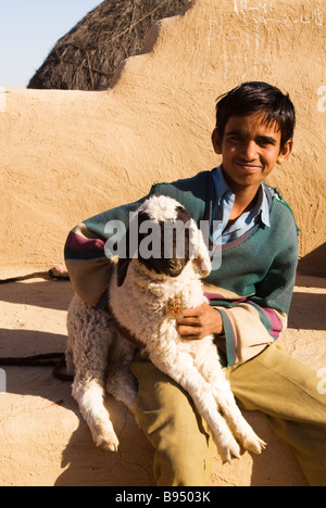 Tenant son agneau bébé près de sa maison dans un village du désert du Rajasthan. Banque D'Images