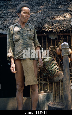 Guerre du Vietnam Central Highlands Montagnard Hill Tribe homme debout à côté de la hutte au toit de chaume à Dak Pek Camp de Base des Forces spéciales Banque D'Images