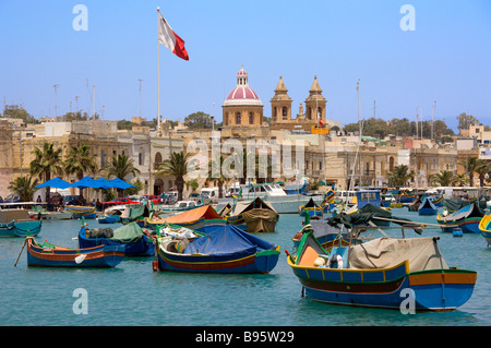 Malte Marsaxlokk Harbour bateaux colorés et église Notre Dame du Rosaire à côte sud village de pêcheurs avec pavillon maltais Banque D'Images