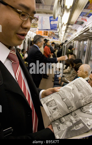 Le Japon Honshu Tokyo jeunes Japonais homme portant un costume montrant la bande dessinée manga il est relevé sur le métro de Tokyo Banque D'Images
