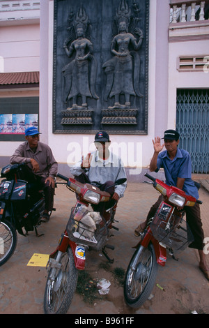 Cambodge Siem Reap trois chauffeurs de taxi moto sur leurs cyclomoteurs sous une grande plaque murale montrant deux Apsaras. Banque D'Images