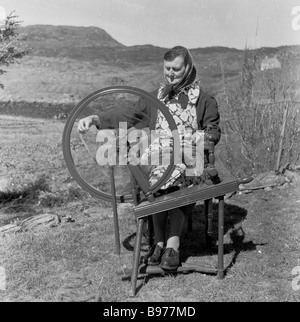 1950s, historique, une vieille femme de crofter écossaise assise travaillant une roue en bois pour faire tourner de la laine à l'extérieur sur son croft, Highlands, Écosse, Royaume-Uni Banque D'Images