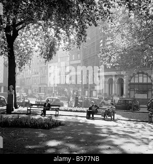 Des gens assis sur des bancs bénéficiant d'un emplacement paisible au soleil à Leicester Square, le West End de Londres dans cette photo par J Allan des espèces dans les années 1950. Banque D'Images