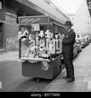 1960s, un marchand de rue vendant des jouets mous, des souvenirs et des nouveautés à partir d'un stand portatif dans une rue latérale de Londres Leicester Square, Angleterre, Royaume-Uni. Banque D'Images