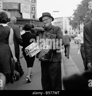 Bus de rue âgé, 1950s. Un ancien militaire ou un soldat handicapé jouant une boîte de pression dans la rue à Leicester Square, Londres, Angleterre, Royaume-Uni. Banque D'Images