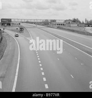 1960s, une voiture sur un sliproad à côté d'une autoroute M1 vide, devant une station de service de Fortes, à Newport Pagnell, la première zone de service de ce type au Royaume-Uni. Banque D'Images