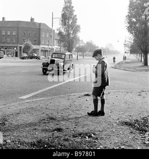 1950s, historique, un écolier debout au coin d'une rue prenant des photos de voitures en mouvement avec son appareil photo Kodak Brownie, Angleterre, Royaume-Uni. Banque D'Images