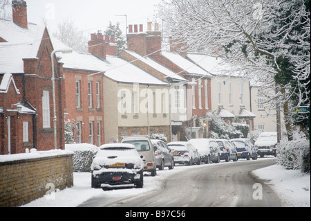 Voitures garées à l'extérieur des maisons sur une route enneigée dans un village d'Angleterre en hiver. Banque D'Images