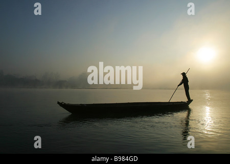 Les palettes d'un homme son canot dans la brume matinale le long de la rivière Rapti bordant le parc national de Chitwan au Népal, Kathmandu. Banque D'Images