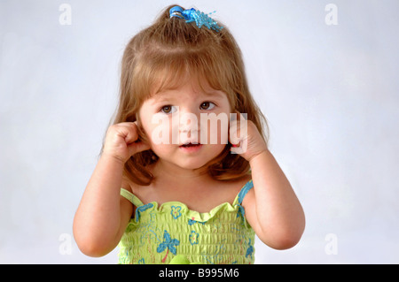 Petite fille hispanique et des tout-petits Les yeux dans l'appareil photo maintenant ses oreilles Banque D'Images