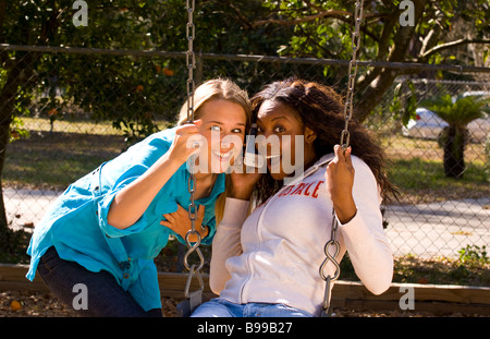 Deux jeunes femmes âgées de 20 ans à jouer avec le swing en plein air dans le parc de rire et s'amuser en jouant avec l'écoute de l'Iphone Banque D'Images