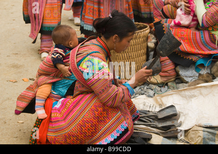 Femme Hmong fleurs colorées et son bébé l'achat d'une pelle dans le marché en cau fils près de Bac Ha Vietnam Banque D'Images