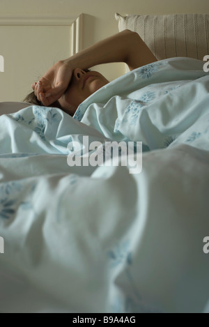 Femme couchée au lit avec le bras sur le visage Banque D'Images
