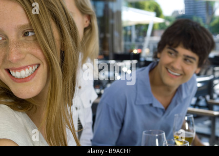 Young Friends sitting at sidewalk cafe, regardant par-dessus les épaules et smiling Banque D'Images