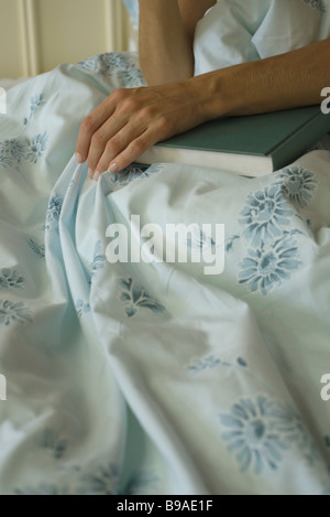 Femme assise au lit avec main reposant sur livre, portrait Banque D'Images
