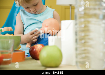 Toddler girl Playing with baby doll à table Banque D'Images