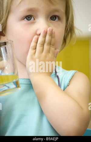 Little girl holding verre de jus, couvrant la bouche avec une main Banque D'Images