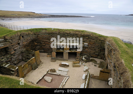 Une des anciennes rotondes excavées au Skara Brae, Orkney, Scotland, avec plage et mer en arrière-plan. Banque D'Images