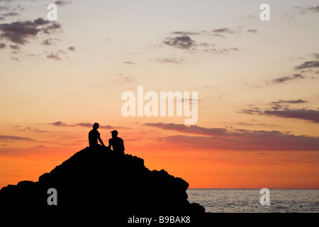 Silhouette d'hommes assis sur les rochers au coucher du soleil à Manuel Antonio, Costa Rica. Banque D'Images