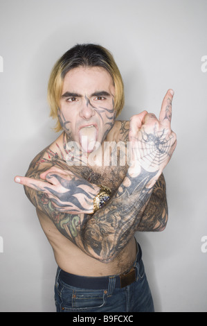 Jeune homme haut du corps sérieusement tinkefinger "tatouages librement' show langue semi-geste portrait gens tatouages tatouage Banque D'Images