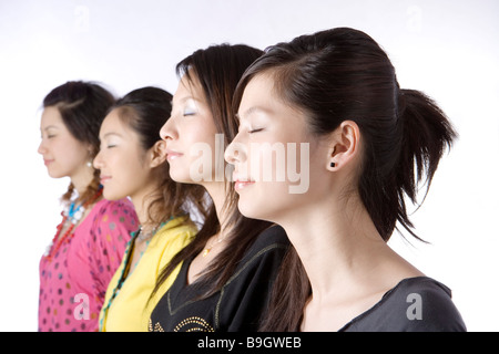 Quatre jeunes femmes standing against white background with closed eyes side view portrait Banque D'Images