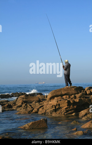 Pêcheur solitaire sur roches côtières Banque D'Images