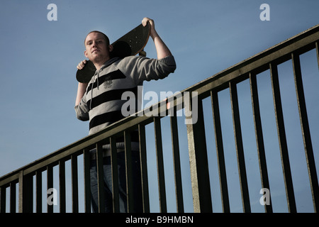 Jeune homme avec une planche à roulettes sur une balustrade Banque D'Images