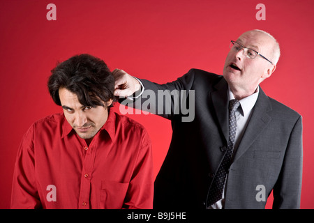 Businessman pulling son assistant's ear Banque D'Images