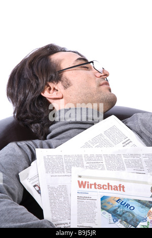 Jeune homme dormir sur un fauteuil en cuir avec un journal Banque D'Images