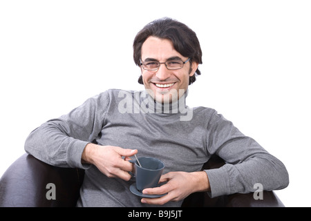 Jeune homme assis sur un fauteuil en cuir avec une tasse de café Banque D'Images