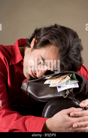 Jeune homme, contenu posée sur son sac plein d'argent Banque D'Images