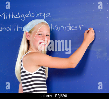 Fille, 11 ans, écrit à la craie sur un tableau noir Banque D'Images