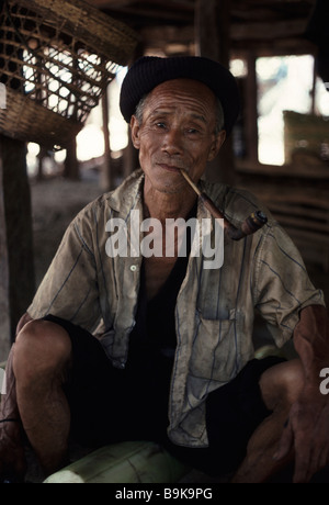 Un vieil homme de la tribu Akha de Thaïlande du Nord, fume sa pipe assis sous sa maison Banque D'Images