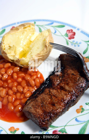 Un steak de surlonge grillé servi sur une plaque avec des haricots blancs à la sauce tomate et une pomme de terre au four garnie de beurre. Banque D'Images