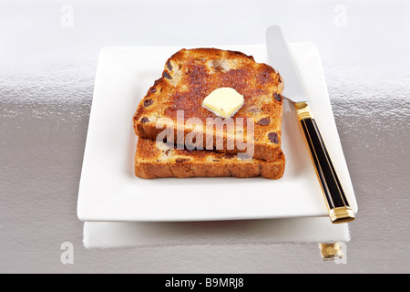 Deux tranches de pain aux raisins avec du beurre et le couteau sur une plaque Banque D'Images